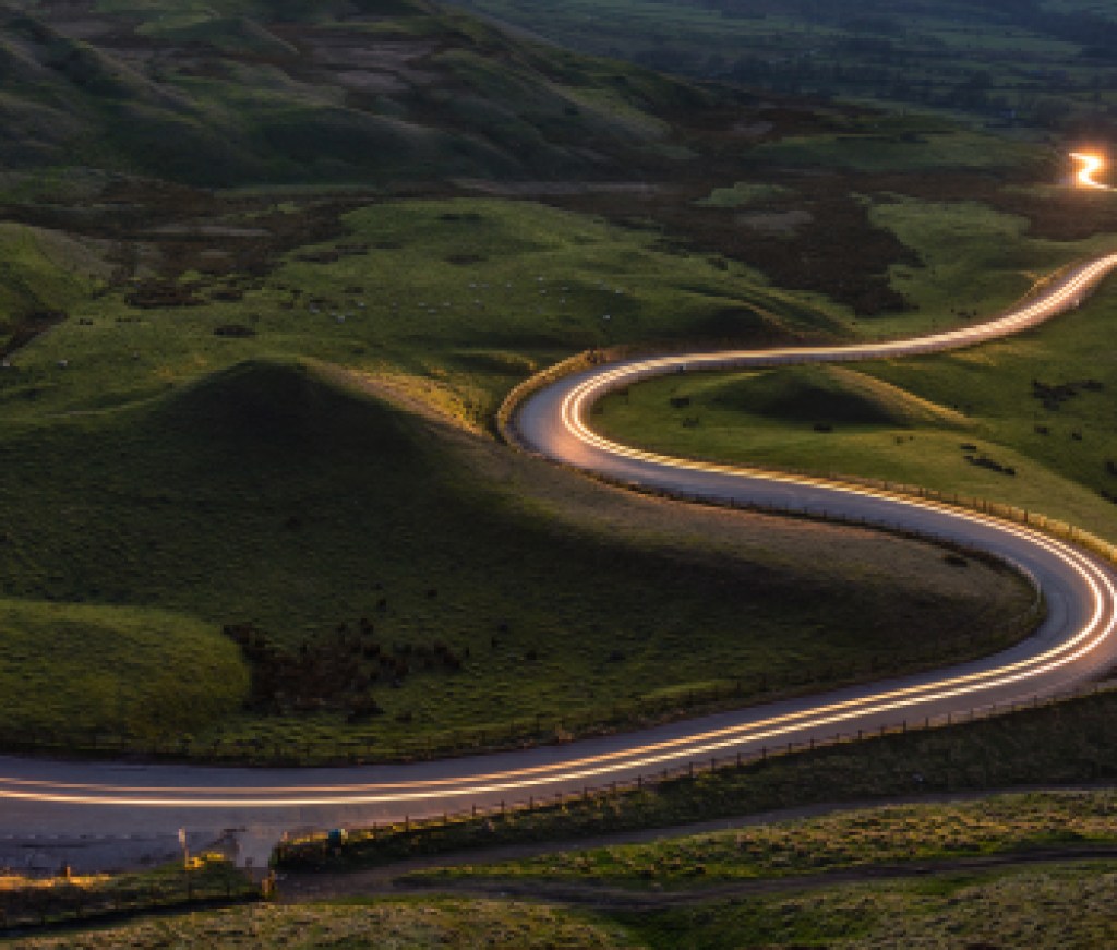 Winding curvy rural road with light trail from headlights leading through British countryside.