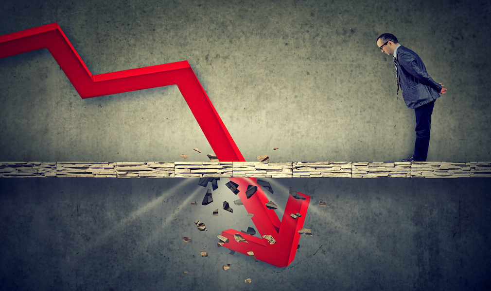 Depressed business man looking down at the falling red arrow going through a concrete floor. Fall and depreciation concept.