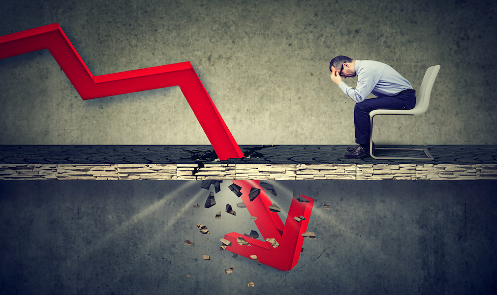 Depressed business man looking down at the falling red arrow going through a concrete floor. Fall and depreciation concept.