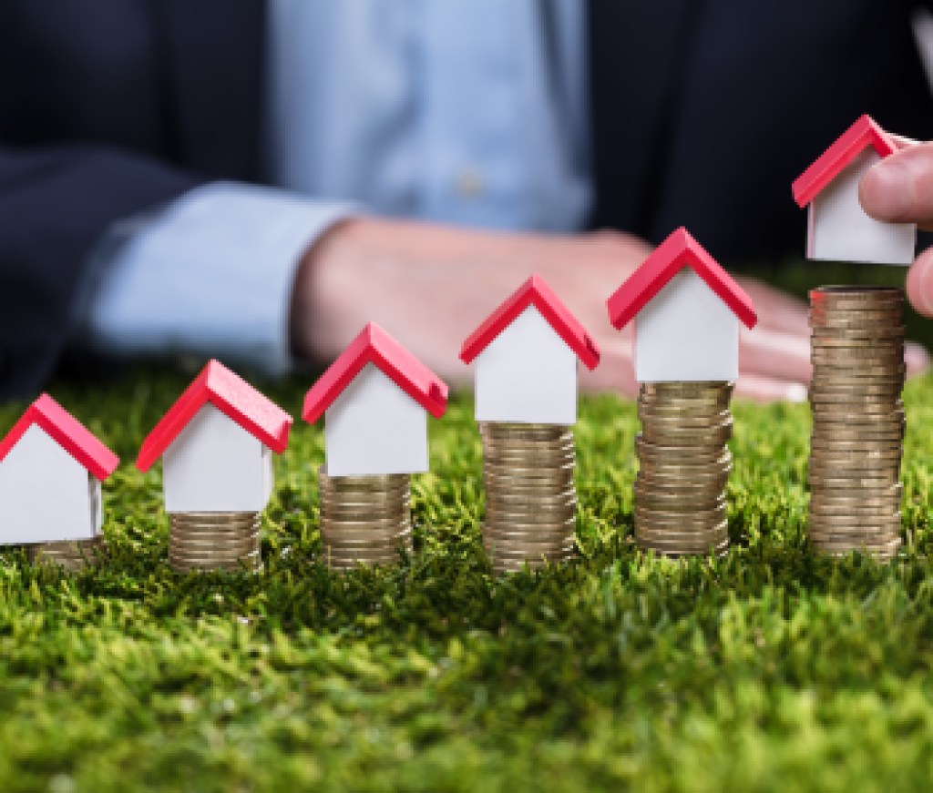 Businessperson Arranging House Model Over Stacked Coins