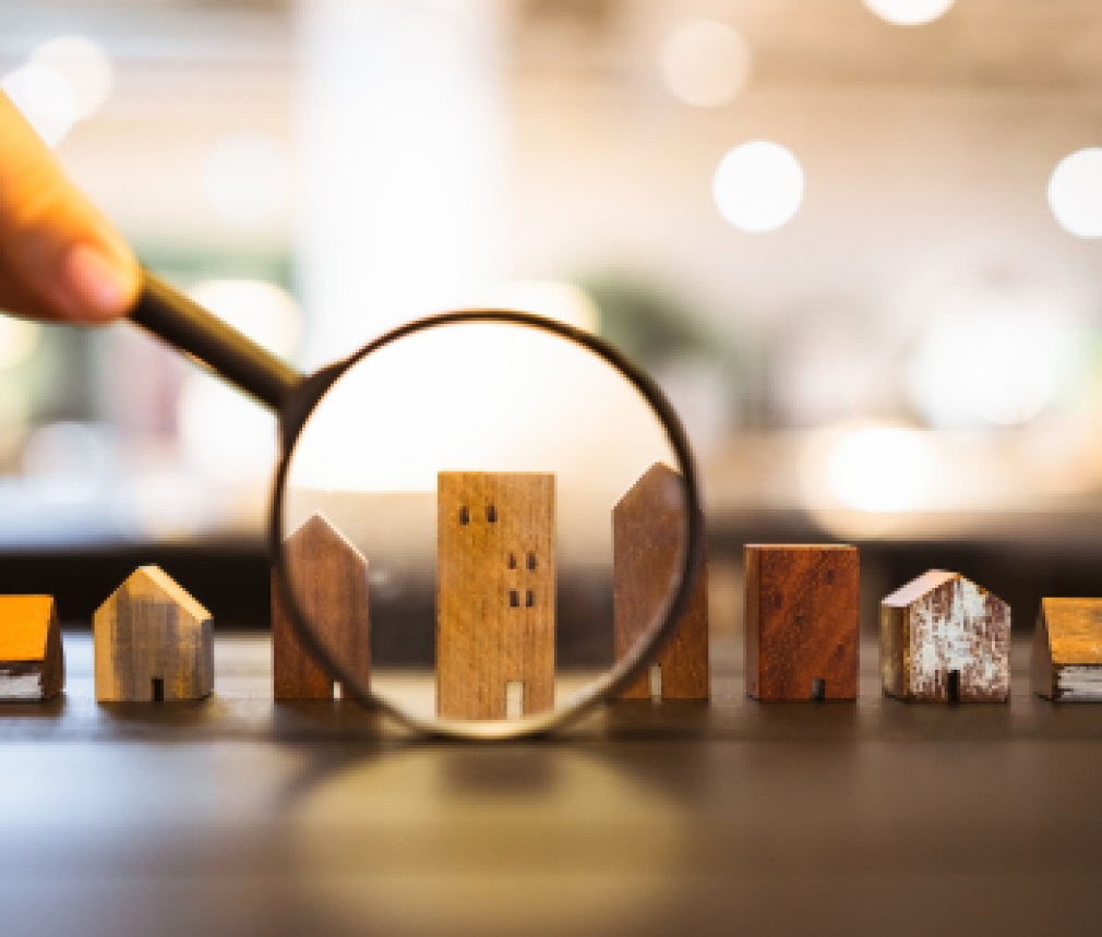 Hand holding magnifying glass and looking at house model, house selection, real estate concept.