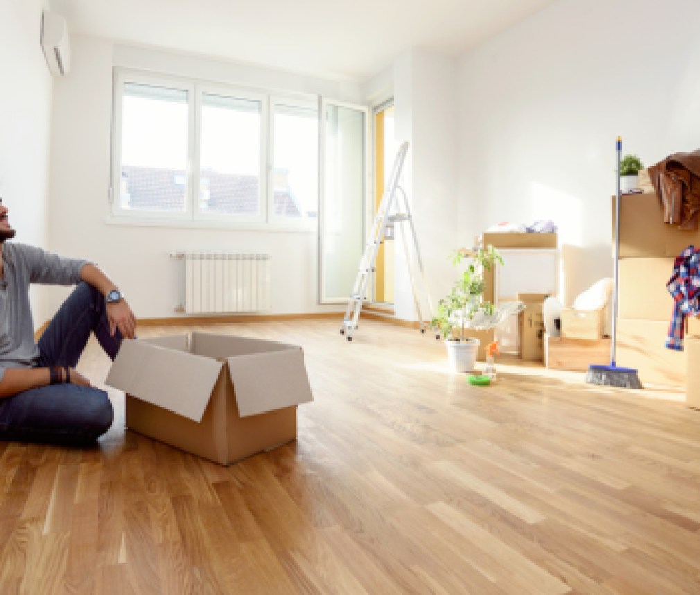 Happy young man just moved into new home unpacking boxes sitting on the floor