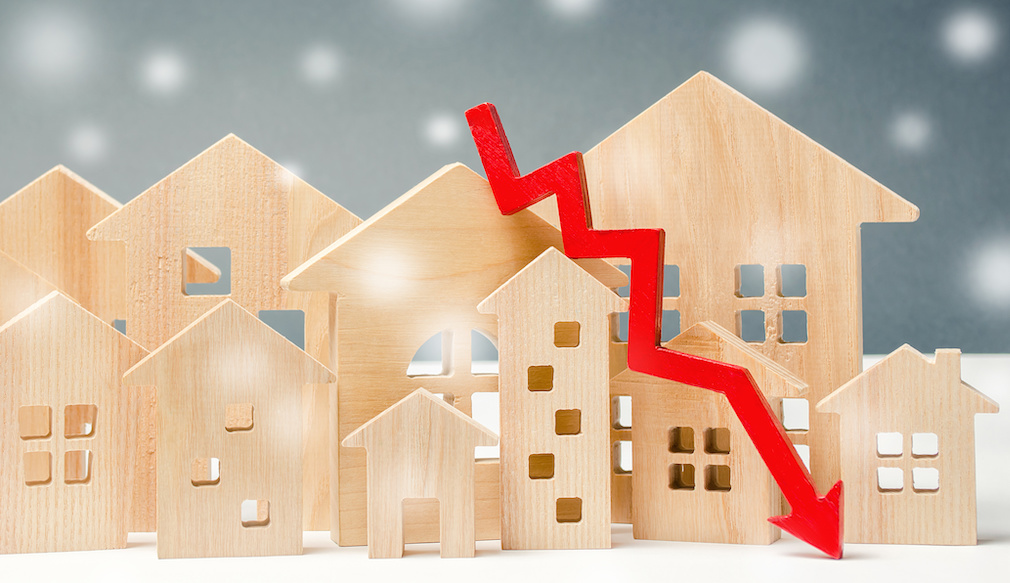 Miniature wooden houses and down arrow. The concept of low housing demand. Discounts for real estate in the winter. Mortgage, loan. Cheap cost. Christmas Snowflakes
