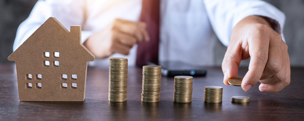 Save to real estate, property owner get money to home concept, small wooden house model on table with hand stacked coins to rent or buy above mentioned residence with cash to bank agency