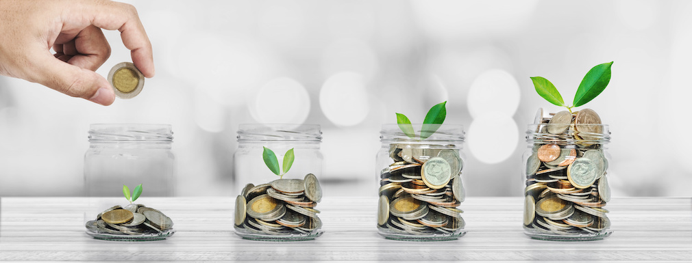 Hand putting coin in glass bottles with plants glowing, Saving money and investment  concepts