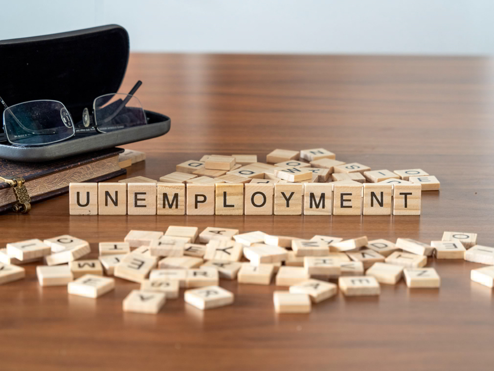 unemployment concept represented by wooden letter tiles on a wooden table with glasses and a book