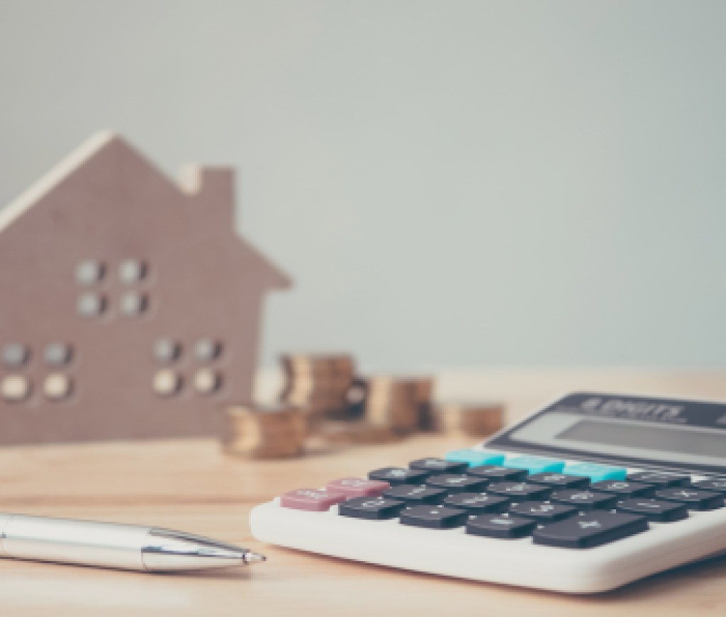 Calculator with wooden house and coins stack and pen on wood table. Property investment and house mortgage financial concept