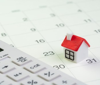 House mortgage payment and installment schedule concept, small miniature house on end of month calendar with calculator
