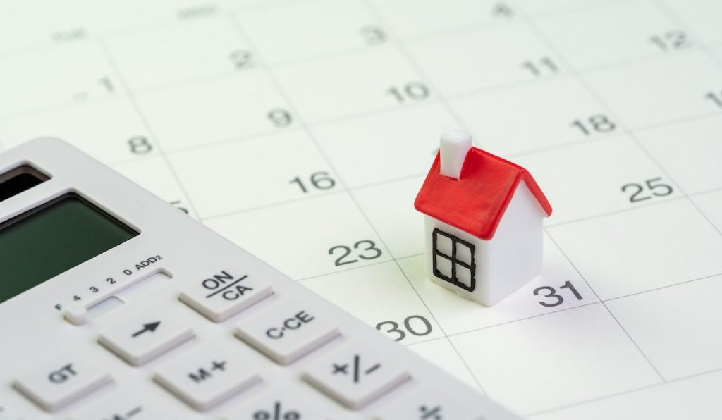 House mortgage payment and installment schedule concept, small miniature house on end of month calendar with calculator