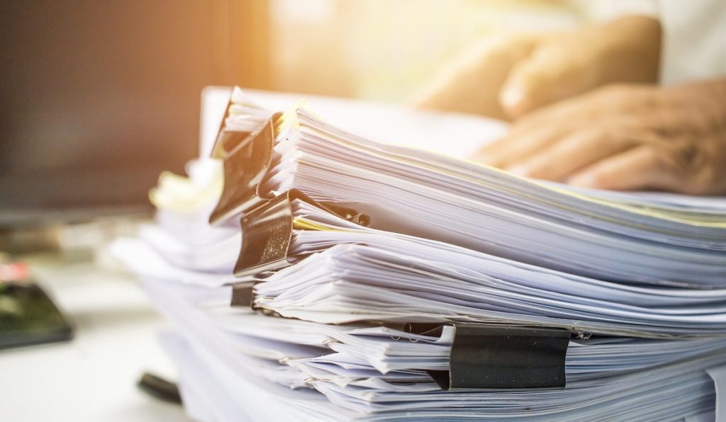 Businessman hands searching data information in Stack of papers files on work desk in office, business report paper or piles of unfinished documents achives with clips on offices indoor, Business concept