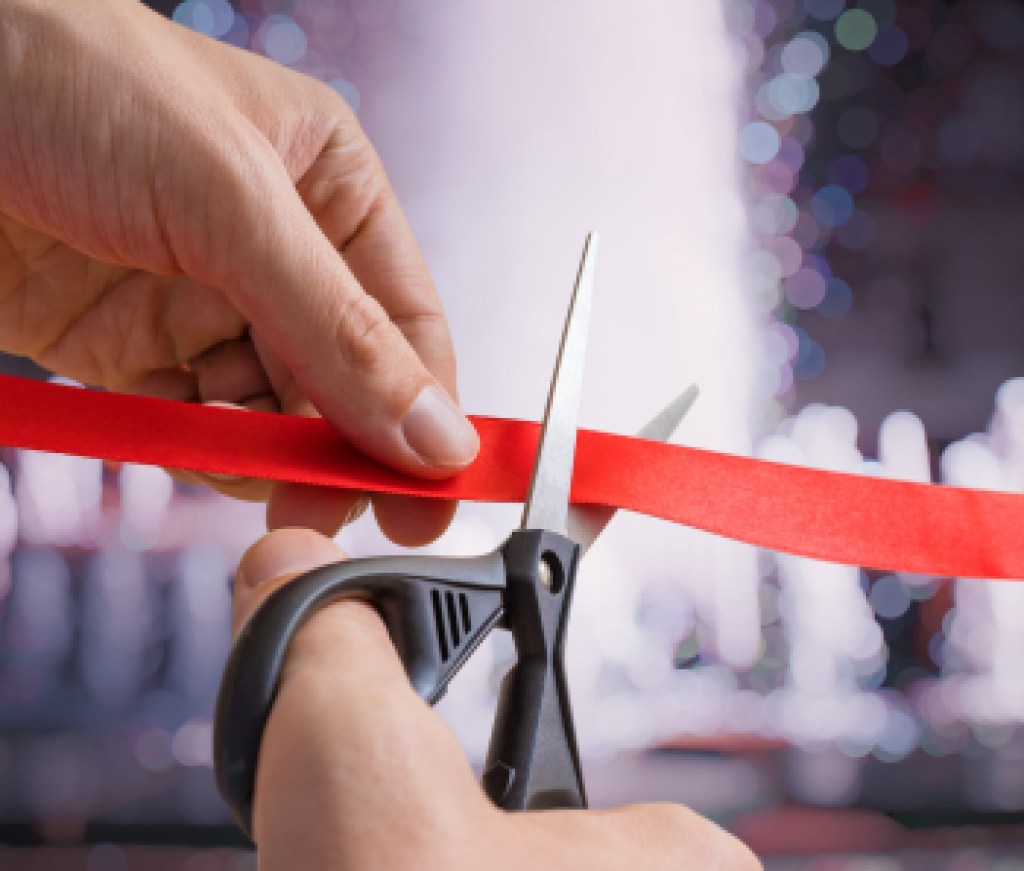 Man is cutting red tape or ribbon against defocused background.