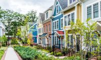 Row of colorful, red, yellow, blue, white, green painted residential townhouses, homes, houses with brick patio gardens in summer
