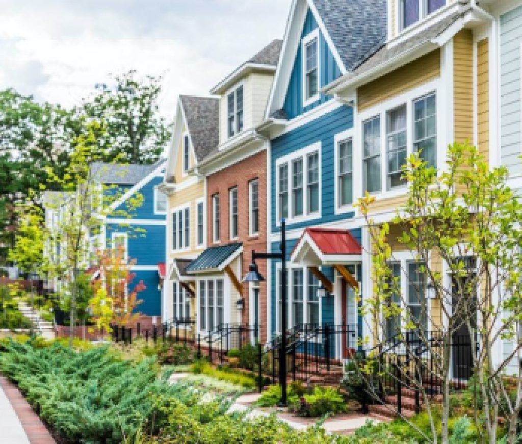 Row of colorful, red, yellow, blue, white, green painted residential townhouses, homes, houses with brick patio gardens in summer