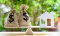 a house and bags of money balancing on a scale