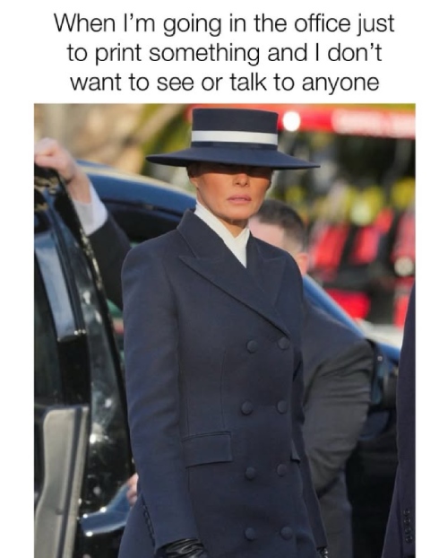 woman standing outside a black SUV wearing an all black suit and a black hat.