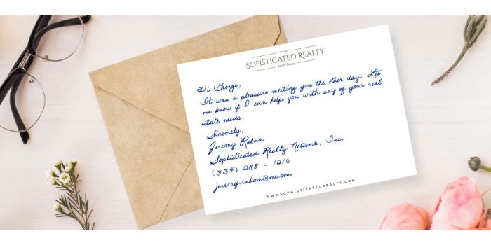 Brown envelope with a white handwritten postcard laying on top surrounded by flowers and a pair of reading glasses.
